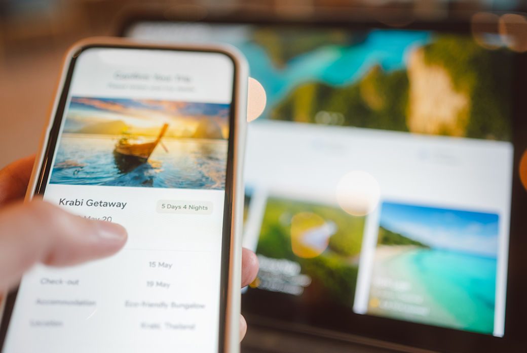 Person comparing tropical vacation options on a smartphone and laptop