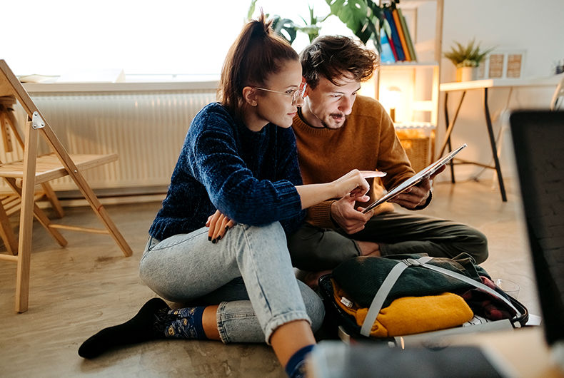 Couple planning a trip on a tablet beside an open suitcase